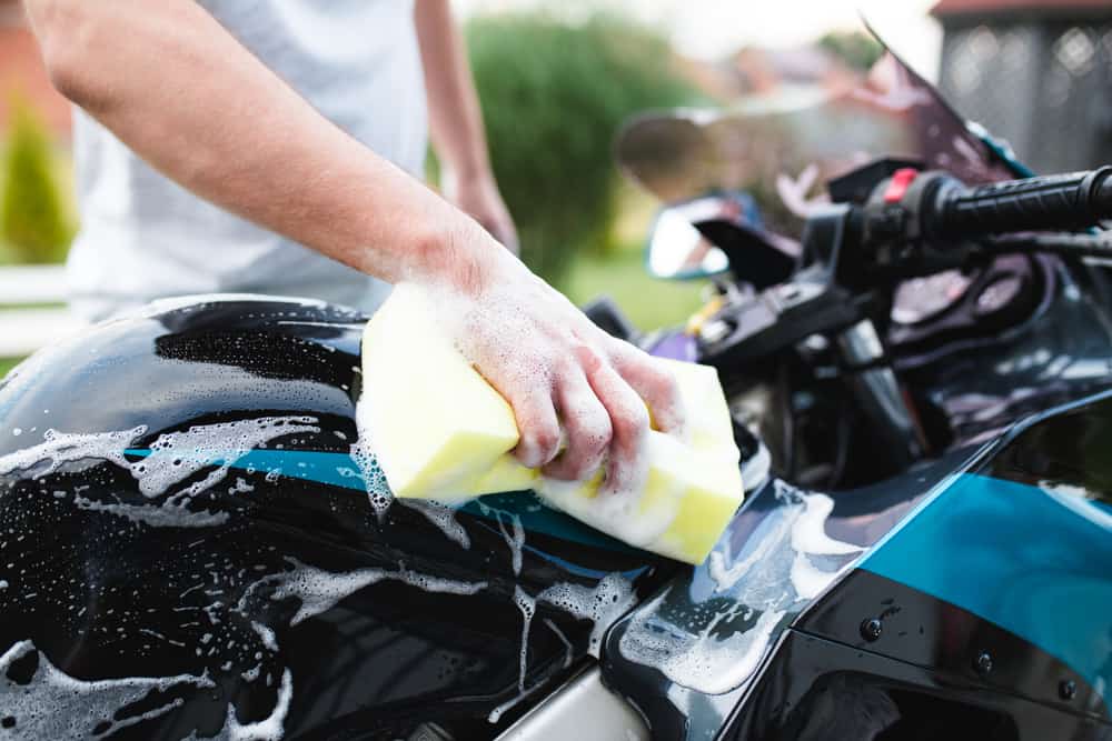 man washing a motorcycle with a soap and sponge.