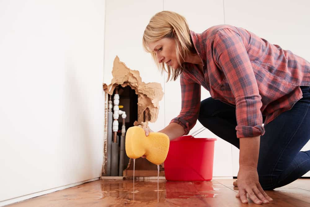 woman cleaning up water from a pipe leak with sponge and fixing it with home insurance