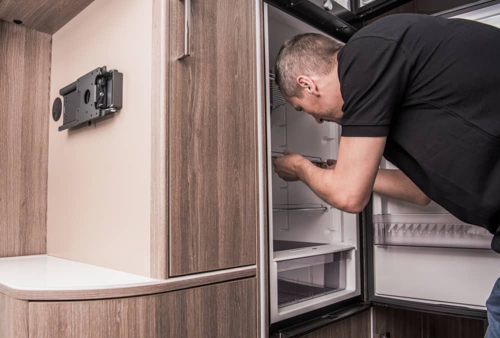 backview of a man giving maintance to a motorhome refrigerator