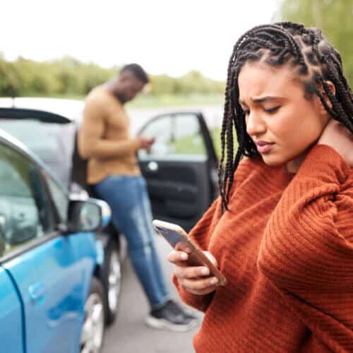 young african american woman looking at smarphone worried with a car accident in the back