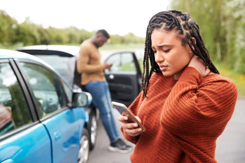 young african american woman looking at smarphone worried with a car accident in the back