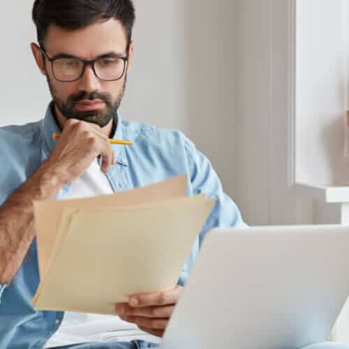 hispanic man thinking and looking at a paper reading a car insurance policy