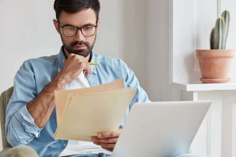 hispanic man thinking and looking at a paper reading a car insurance policy