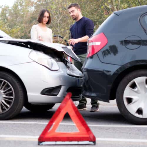man and woman during a car accident talking in the background with an emergency sign on the foreground