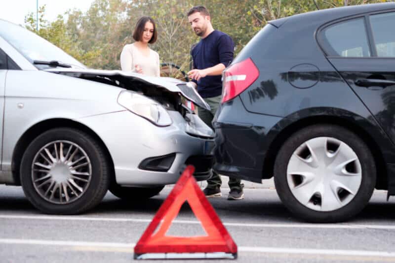 man and woman during a car accident talking in the background with an emergency sign on the foreground