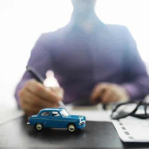 toy car representing car insurance with a man signing a paper in the background
