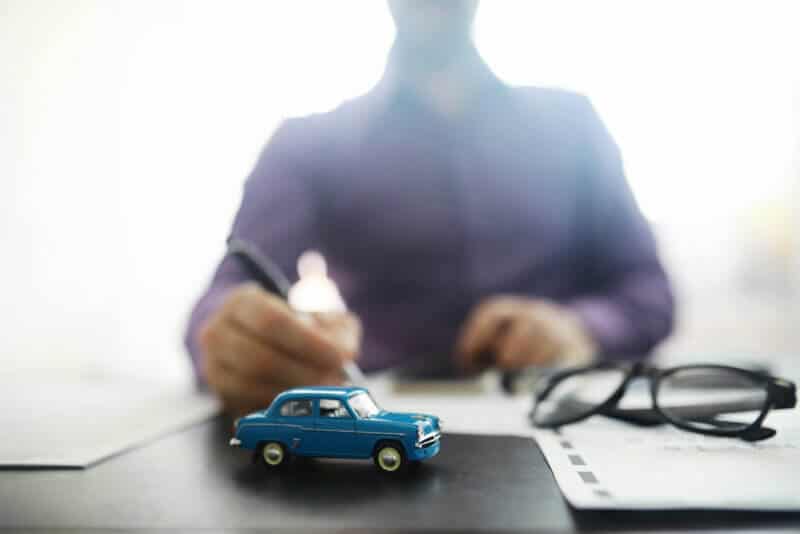 toy car representing car insurance with a man signing a paper in the background