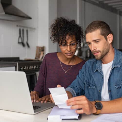 couple in the kitchen looking at paper bill with laptop