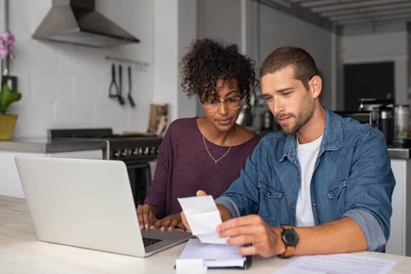 couple in the kitchen looking at paper bill with laptop