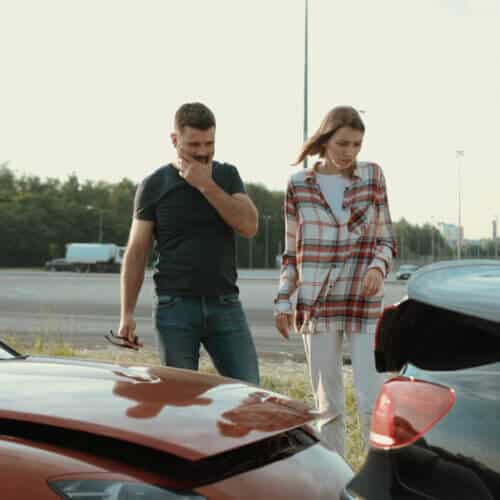 Upset man and woman looking on broken stuck cars after car accident.