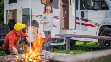 Father and son building a camp fire with an RV in the background