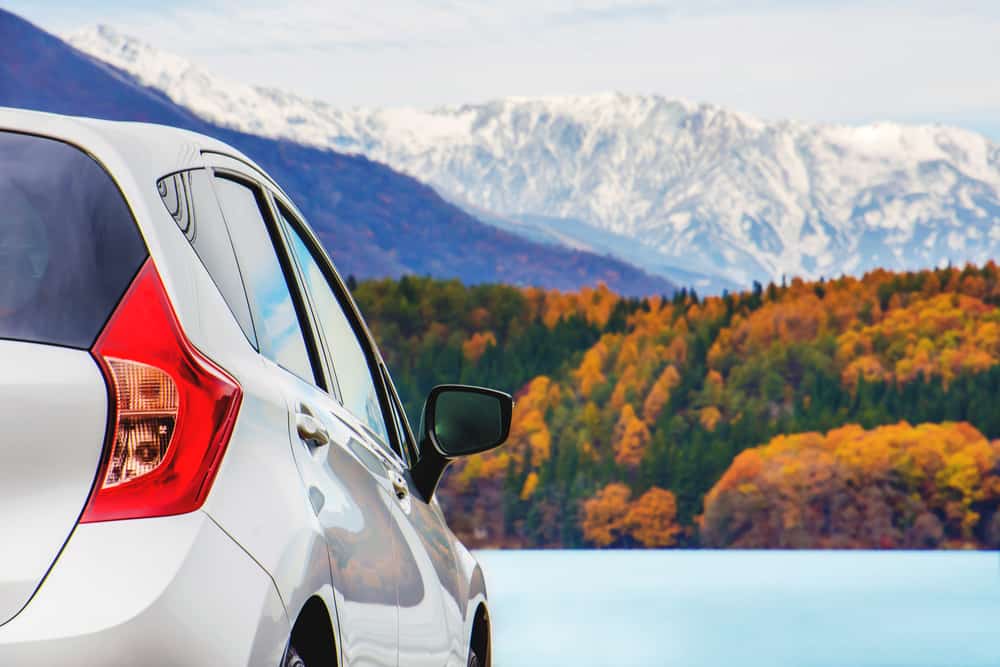 car parked by fall foliage and mountains