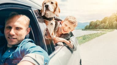 A father drives his son and pet dog down the road