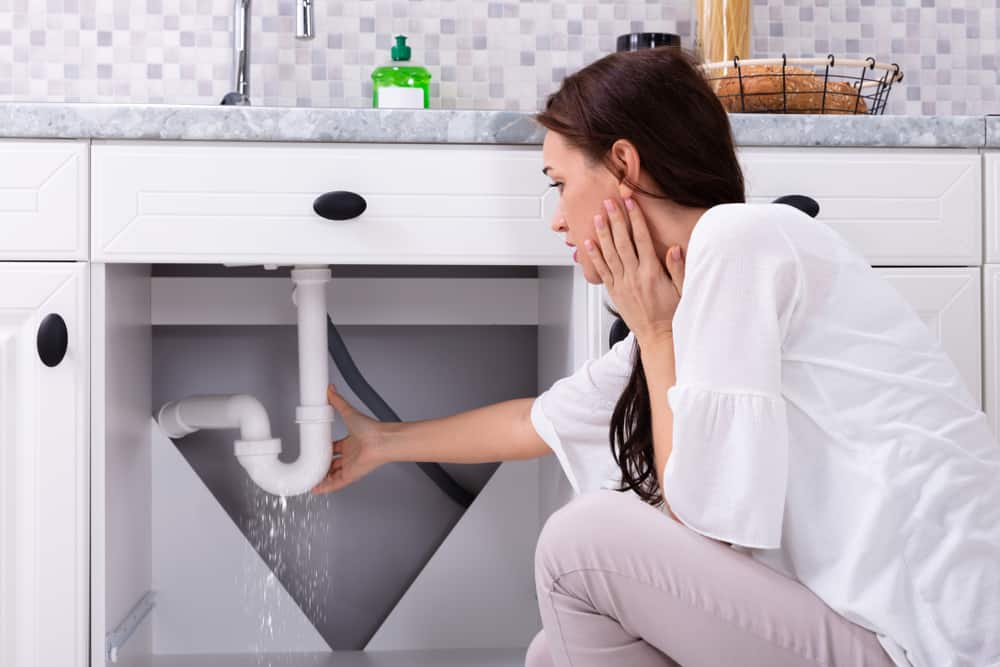 Anxious woman finds a leaking pipe under the sink