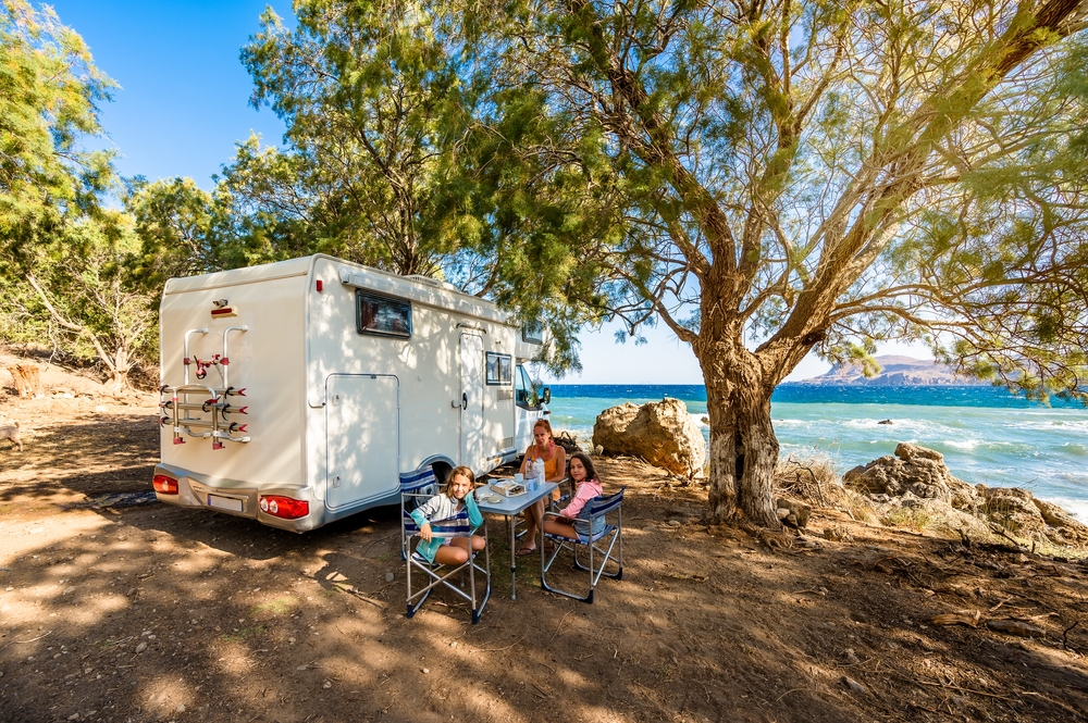 Family camping in their RV under a tree by the water