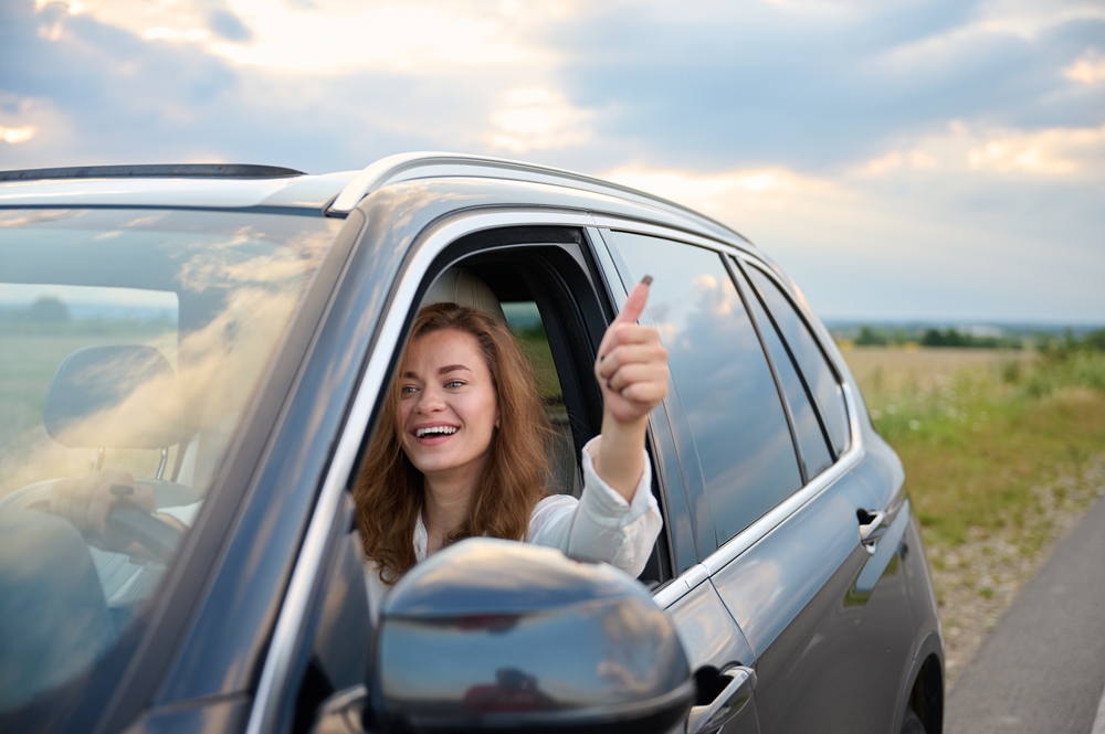 Woman gives thumbs up smiling as she drives