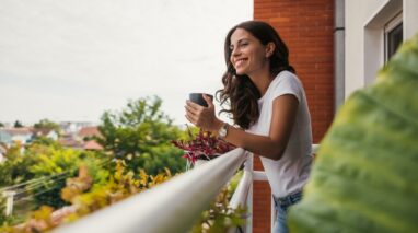 Young woman enjoys a cup of tea while standing on her apartment balcony