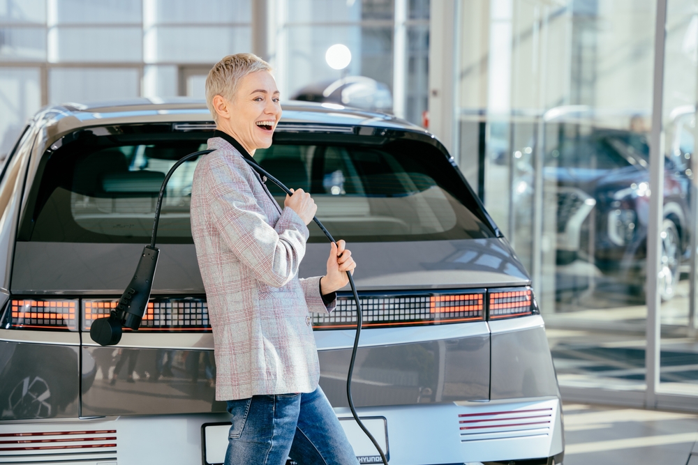 Woman smiling with car's electric cord slung over her shoulder - car insurance in Washington