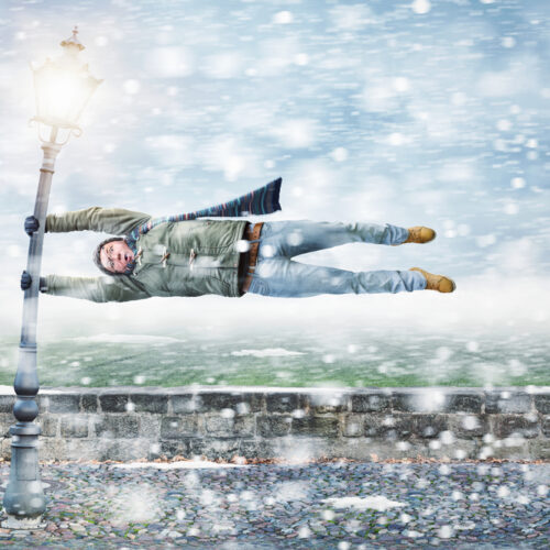Funny picture of man getting blown sideways by winter storn holding on to street pole - cheap home insurance in Washington