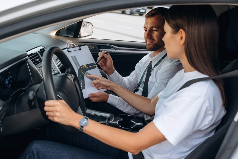 Driving instructor teaching a student inside a car using a diagram, demonstrating techniques learned in a defensive driving course.