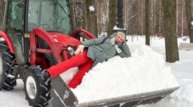 Woman lays in snow in the shovel of a snow plow.