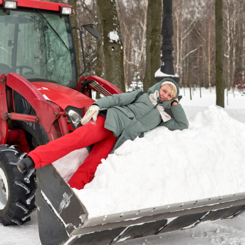 Woman lays in snow in the shovel of a snow plow.