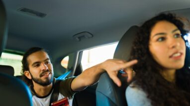 Young rideshare driver listens to instructions from her customer in the back seat who is pointing directions - cheap rideshare insurance in Washington.