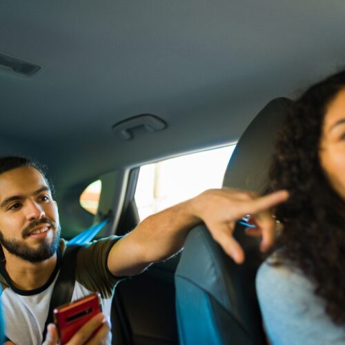 Young rideshare driver listens to instructions from her customer in the back seat who is pointing directions - cheap rideshare insurance in Washington.