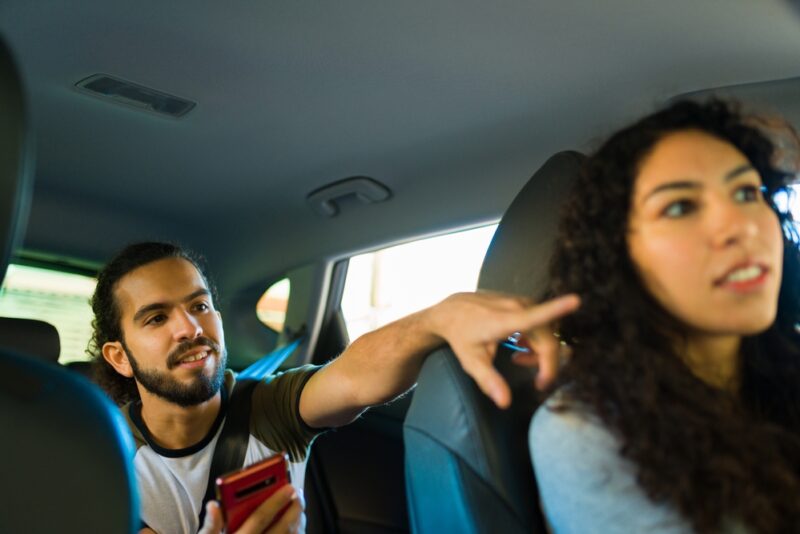 Young rideshare driver listens to instructions from her customer in the back seat who is pointing directions - cheap rideshare insurance in Washington.