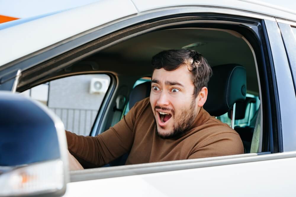 A man making a funny face behind the wheel of the car.