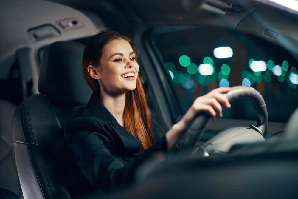 A young woman smiling, driving at night.