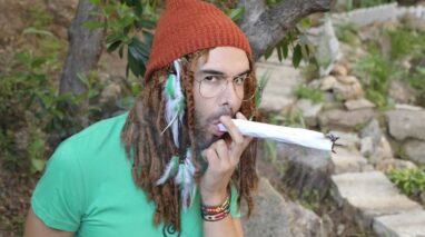 Man with dreads smoking a huge, rolled marijuana joint.