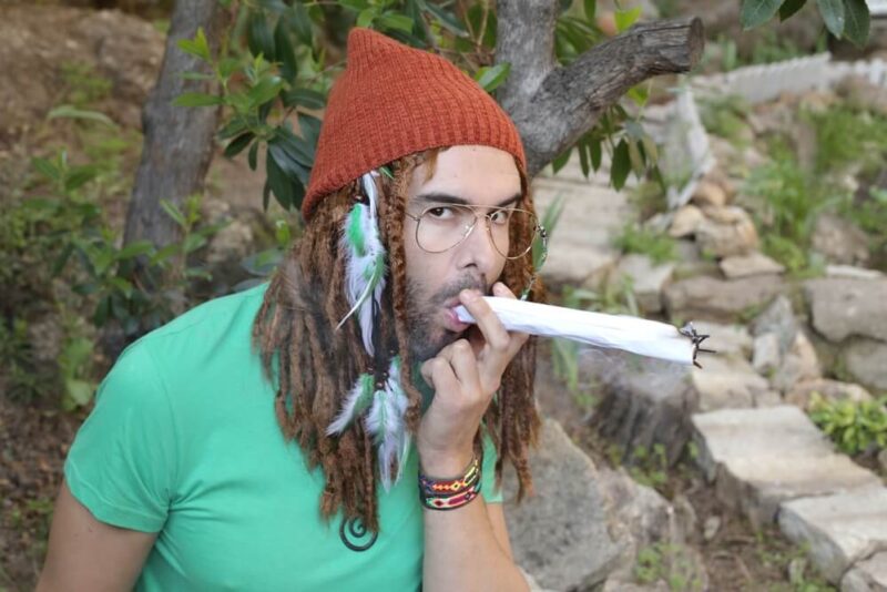 Man with dreads smoking a huge, rolled marijuana joint.