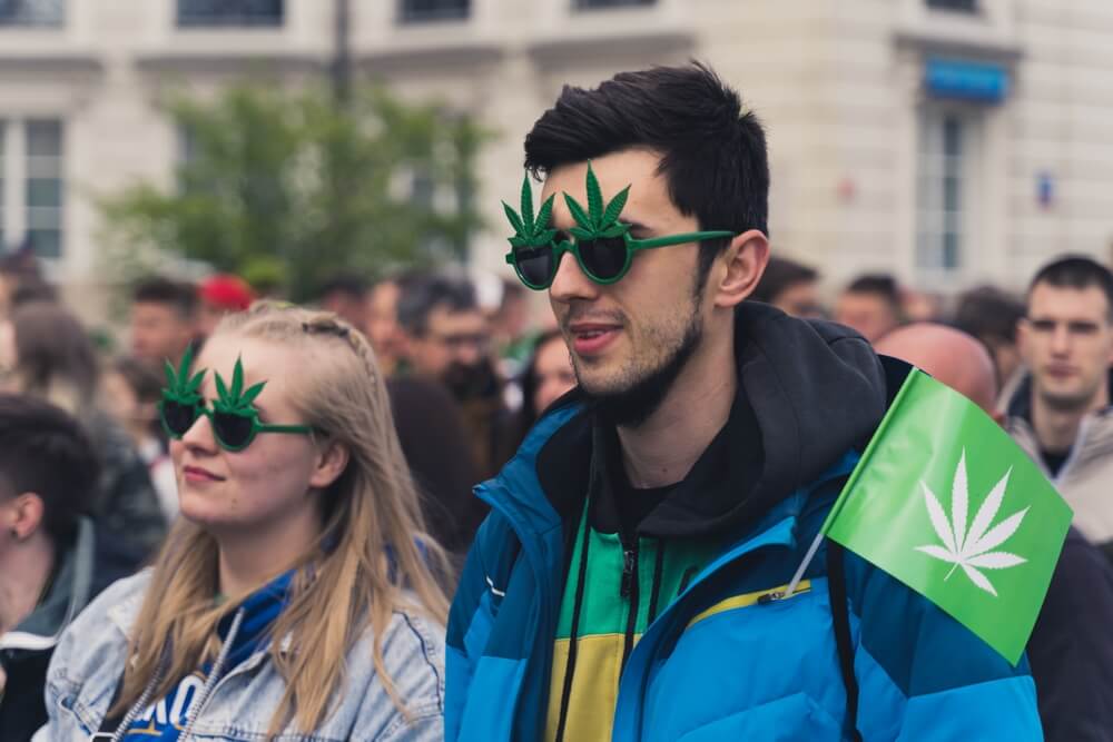 Man and woman walking down the street with sunglasses that have marijuana leaves on them.