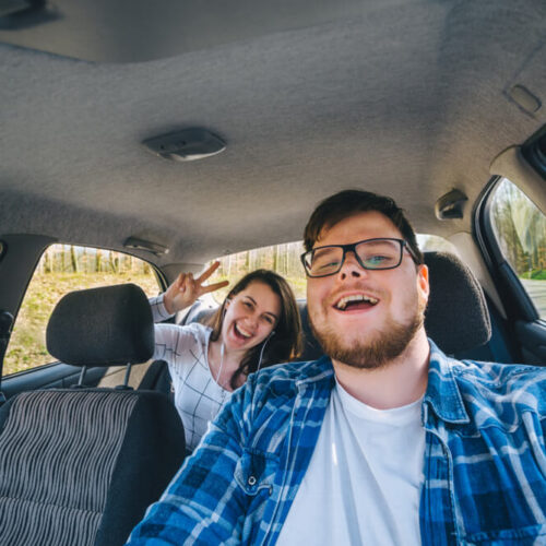 Man laughing behind wheel of car while woman looks on from back seat, concept of insuring someone else's car - cheap car insurance in Washington.