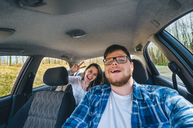Man laughing behind wheel of car while woman looks on from back seat, concept of insuring someone else's car - cheap car insurance in Washington.