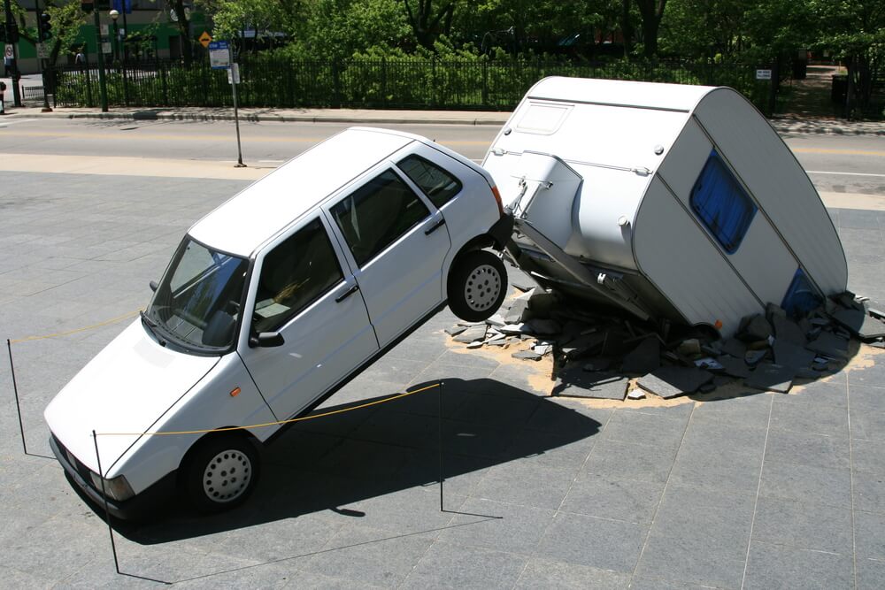 Small car crashes into a damaged travel trailer in a staged scene, showing why trailer insurance in Washington can matter for unexpected towing accidents.