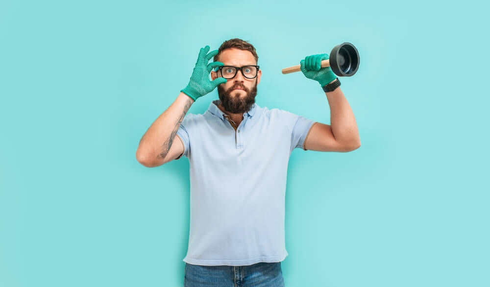 Funny guy in glasses wears gloves and has a plumbing plunger in his hand - cheap home insurance in Washington.