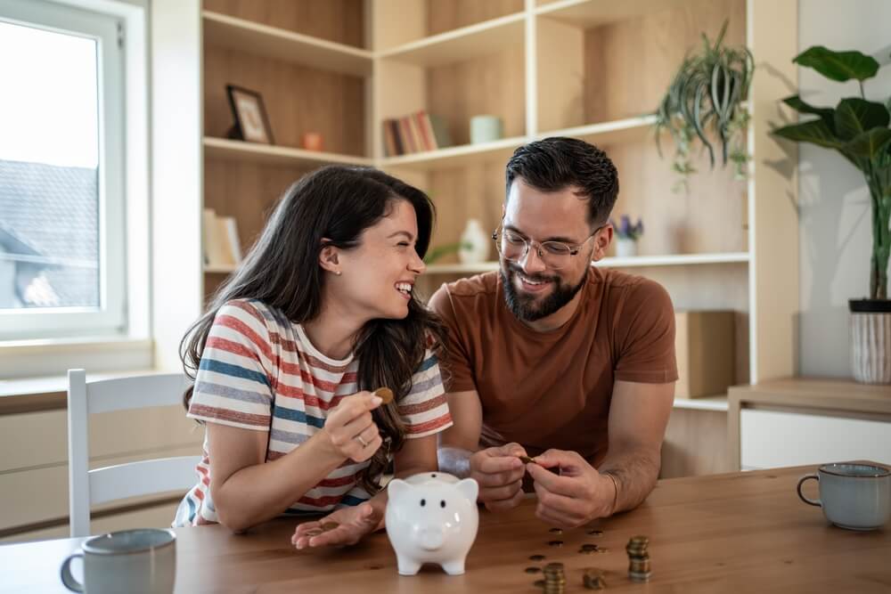 Couple counting savings at home with piggy bank, representing the financial benefits of bundle insurance policies.