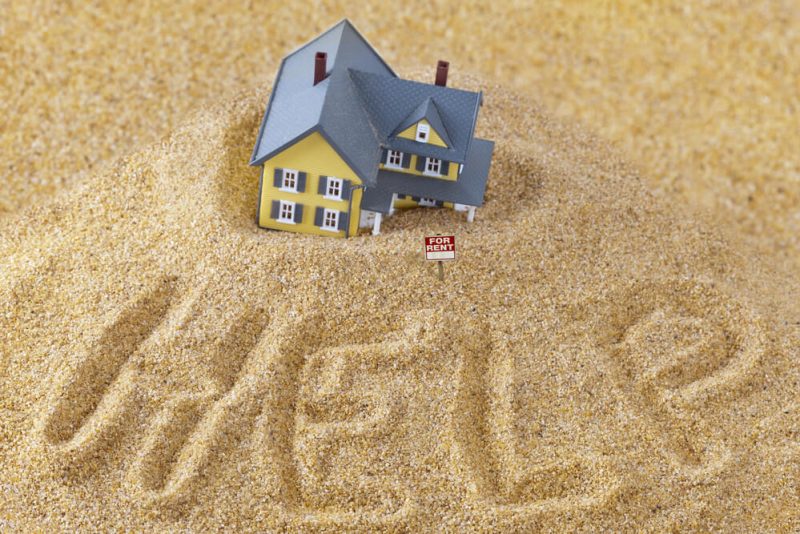 Place house sinking into sand with the words help in the sand and for rent sign - cheap home insurance in Seattle.