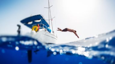 Young man jumps into the sea from the sail boat, image split over under image with the crystal clear sea, cheap boat insurance for protection.