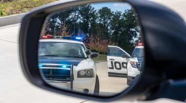 Two police vehicles stop a sedan on a traffic stop, concept of SR-22 insurance.