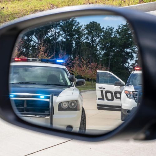 Two police vehicles stop a sedan on a traffic stop, concept of SR-22 insurance.