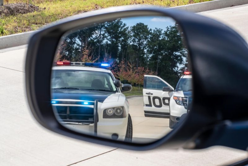 Two police vehicles stop a sedan on a traffic stop, concept of SR-22 insurance.