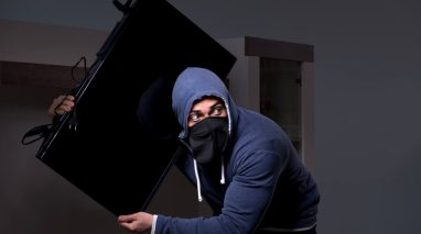 Burglar in black balaclava stealing tv set from house. Burglar or intruder stealing in property apartment. Need for cheap renters insurance in Washington State.