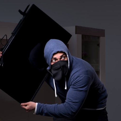 Burglar in black balaclava stealing tv set from house. Burglar or intruder stealing in property apartment. Need for cheap renters insurance in Washington State.