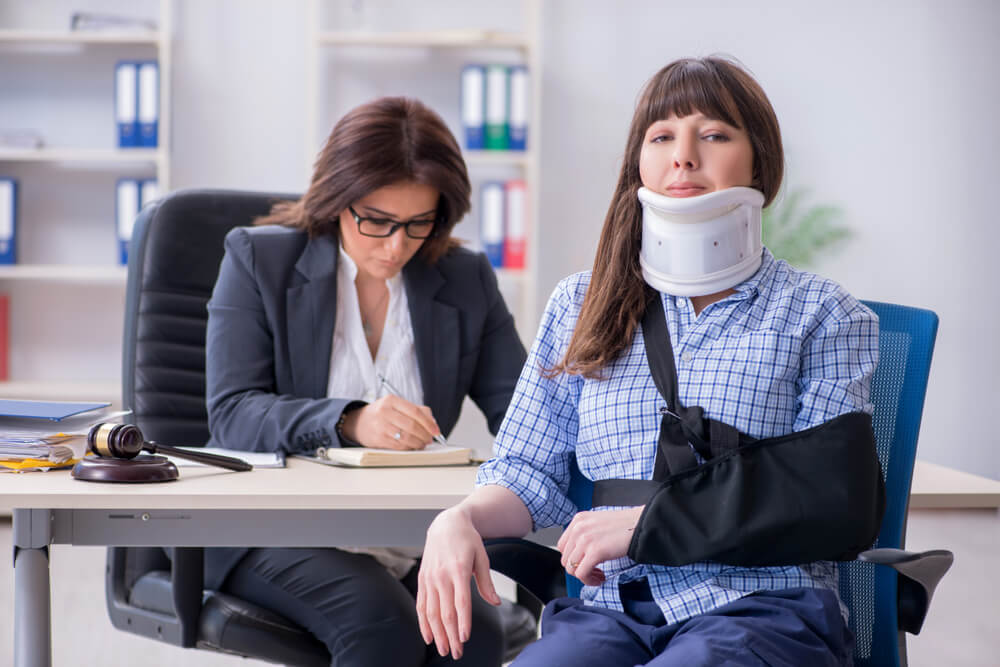 Lady with a neck brace sits in a chair while her lawyer files a suit, protect your business from lawsuit costs with business insurance.