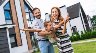 Father and mother play with daughter, pretend she is an airplane, in front of their home in Washington state, insured by cheap home insurance in Washington State.