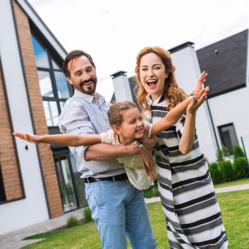 Father and mother play with daughter, pretend she is an airplane, in front of their home in Washington state, insured by cheap home insurance in Washington State.