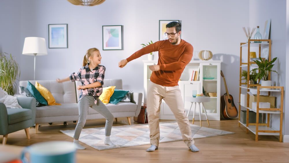 Father and daughter dance in the living room, happy because of low home insurance costs in Washington state.